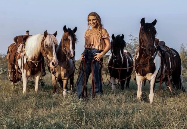 Anna Barker standing in a field, surrounded by 4 horses and ponies